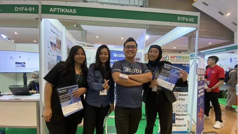 Empat staf Acoba memegang brosur di booth pameran APTIKNAS