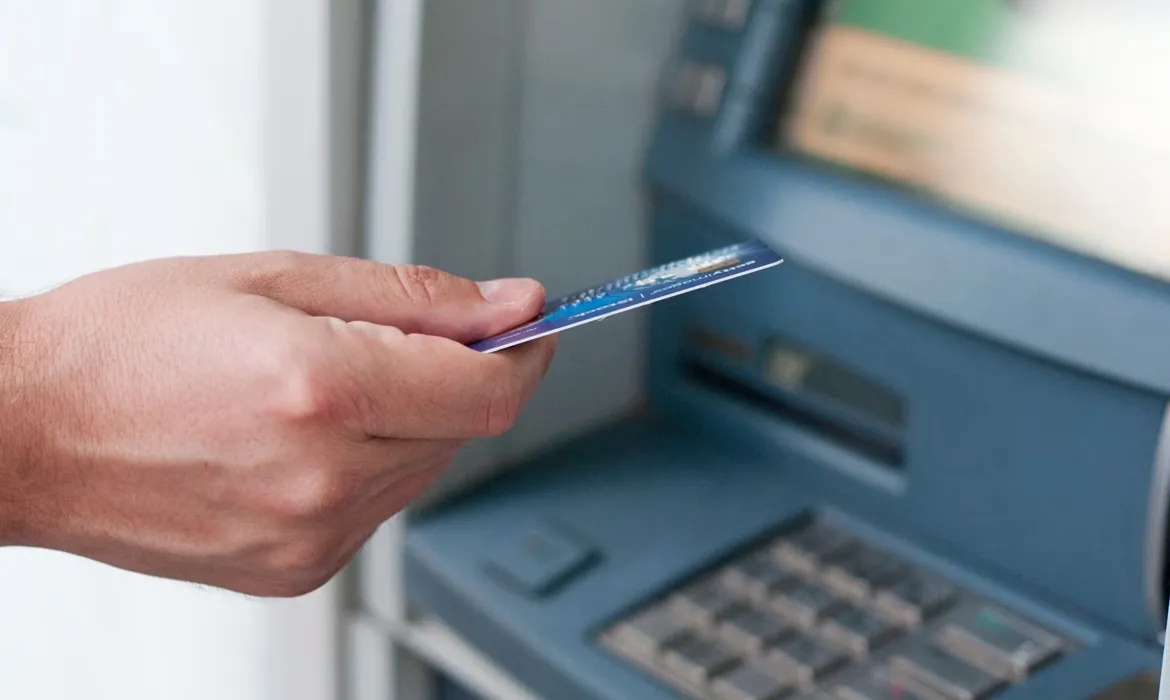Tangan memasukkan kartu debit ke mesin ATM