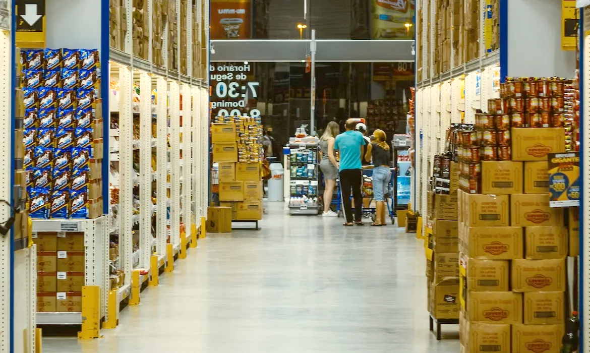 Lorong supermarket dengan rak tinggi dan beberapa pengunjung berbelanja